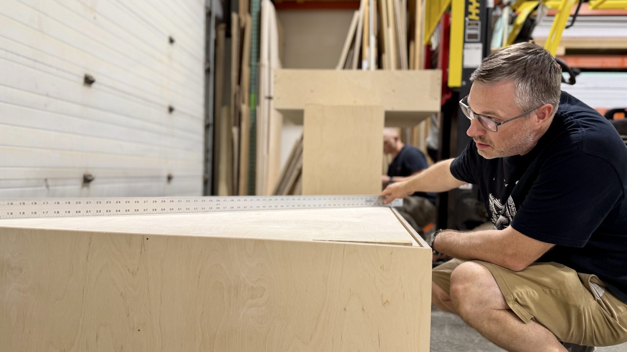 Upland craftsman sighting down a straightedge laid across a pedestal top to check it for deflection