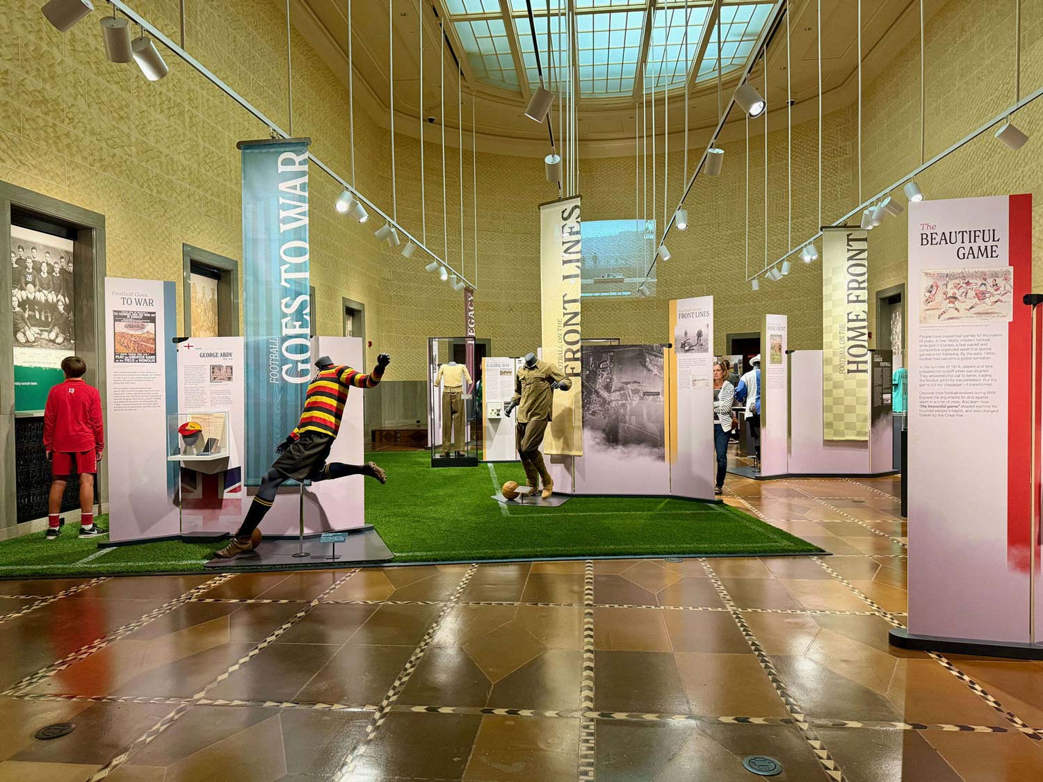 The Beautiful Game and the Great War exhibit in the museum rotunda, with hanging banners over a turf pitch