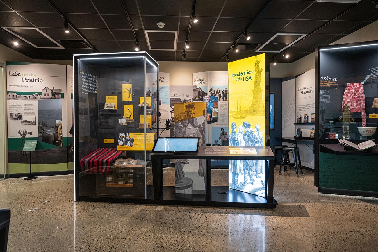 Wide view of the In Search of a Homeland exhibit gallery, with artifact cases and immigration banners